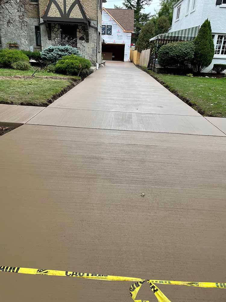 A concrete driveway leading to a house with a yellow caution tape.