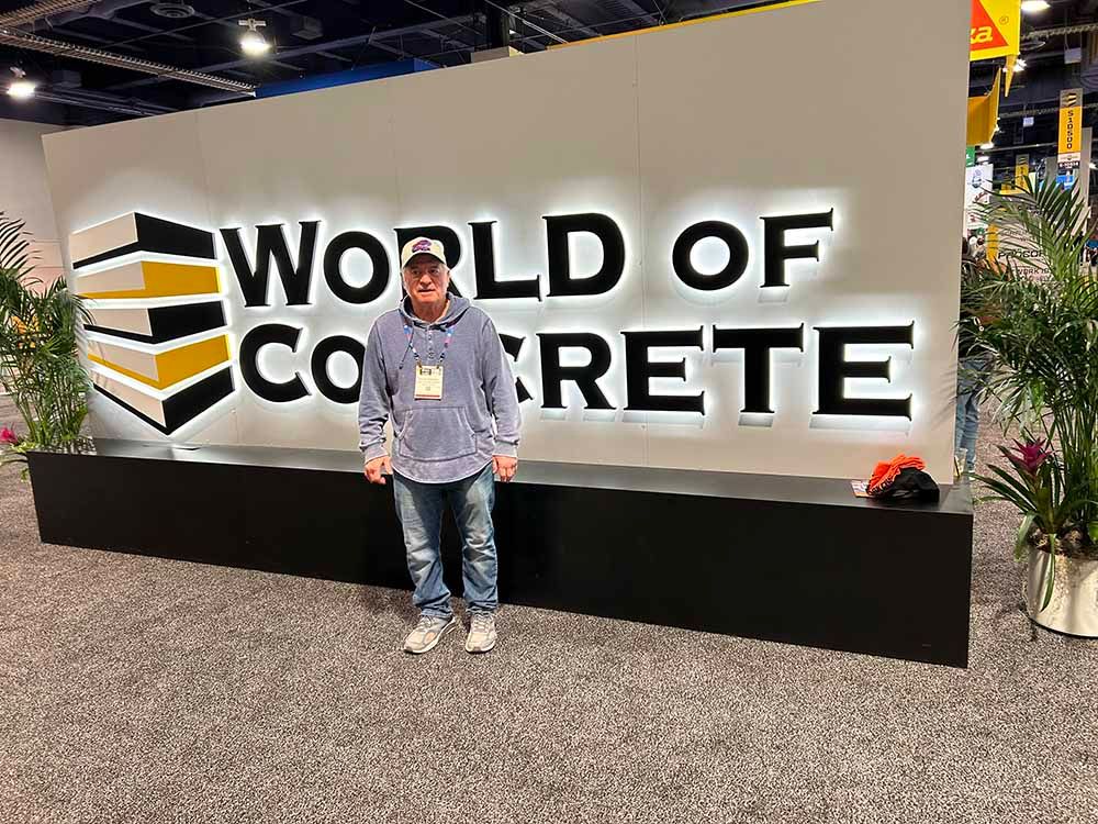 A man is standing in front of a world of concrete sign.