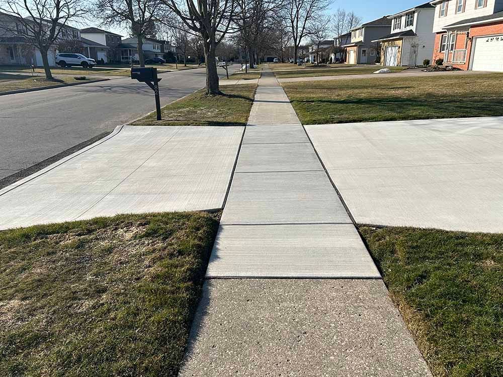 A concrete sidewalk leading to a mailbox in a residential neighborhood.