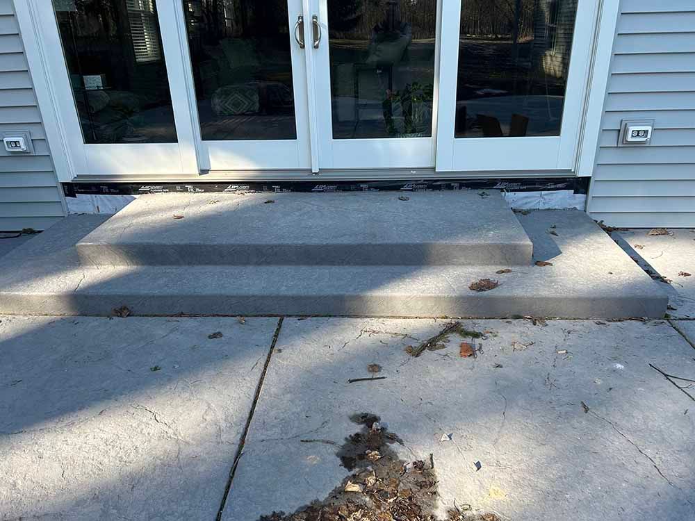 A concrete patio with steps leading up to a house with sliding glass doors.