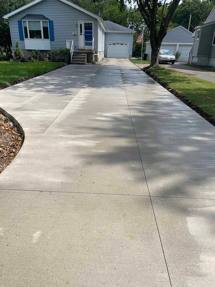 A concrete driveway leading to a house in a residential neighborhood.