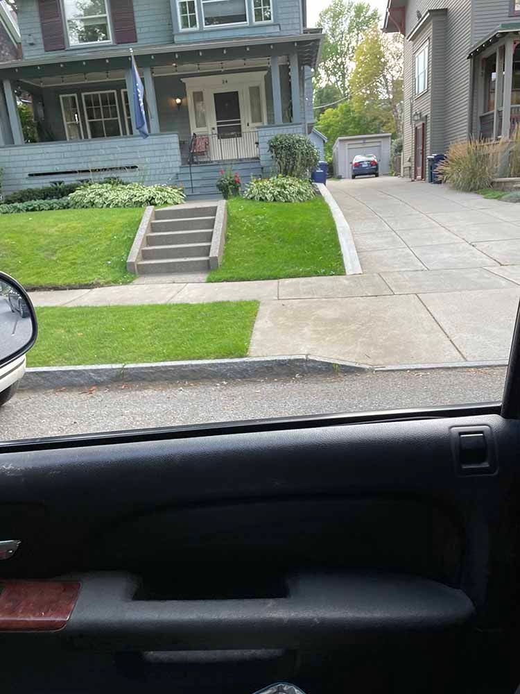 A car is driving down a street in front of a house.