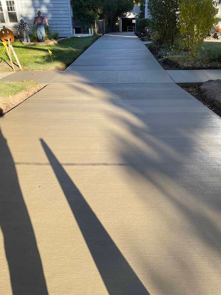 A shadow of a person is cast on a concrete driveway leading to a house.