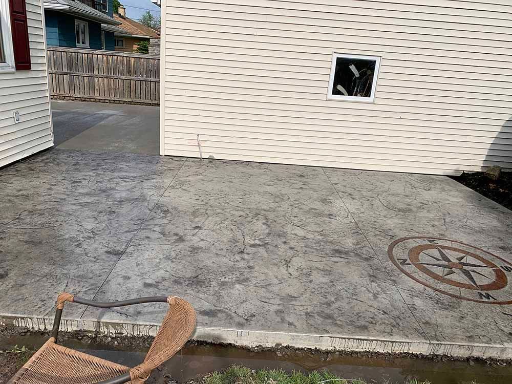 A patio with a chair and a compass on it in front of a house.