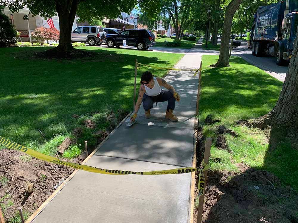 A woman is working on a sidewalk in a park.