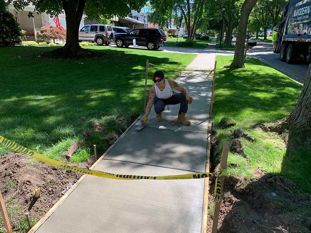 A woman is kneeling down on a concrete sidewalk.