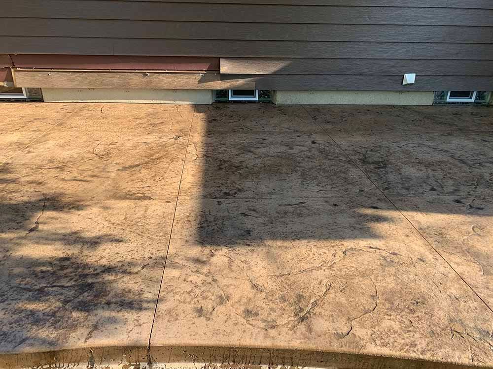 A shadow of a tree is cast on a concrete floor in front of a house.