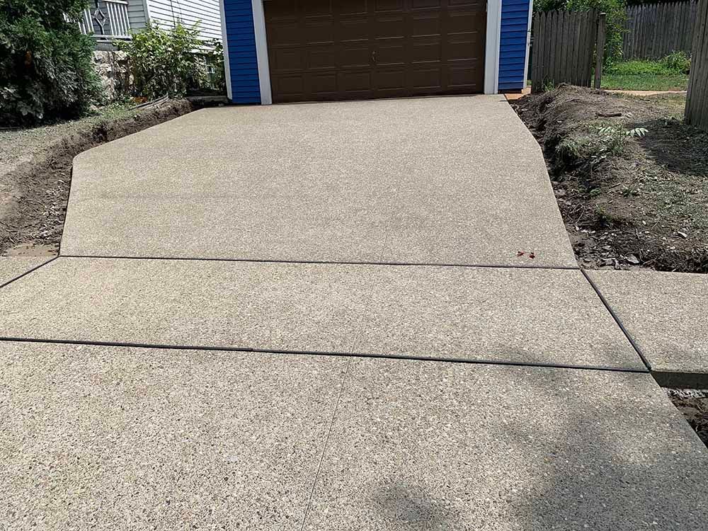 A concrete driveway leading to a garage with a blue house in the background.