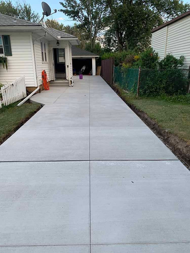 A concrete driveway leading to a white house.