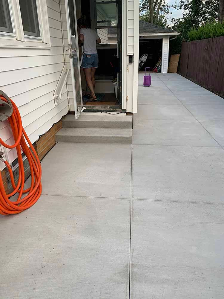 A woman is standing in the doorway of a house next to a hose.