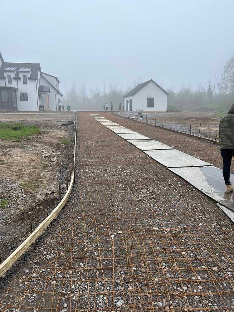 A person is walking down a dirt road in front of a house.