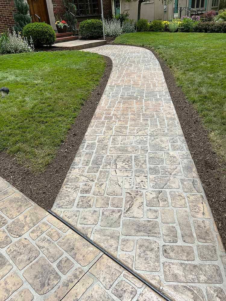 A concrete walkway leading to a house with a lush green lawn.