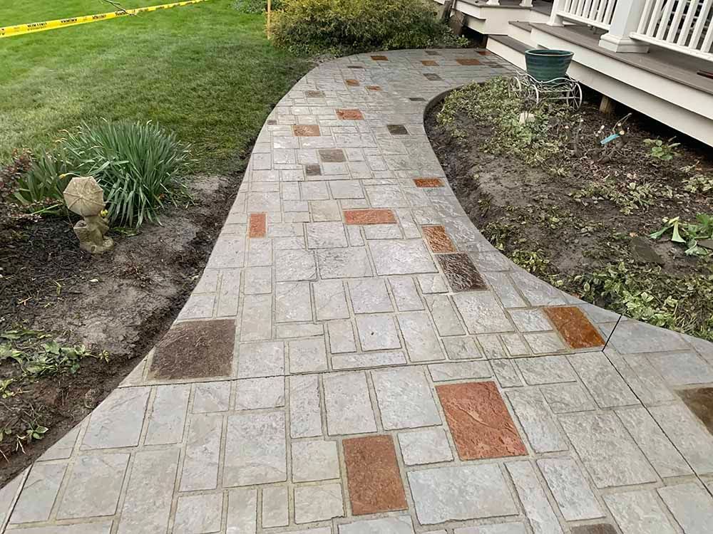 A brick walkway leading to a house with a lawn in the background.