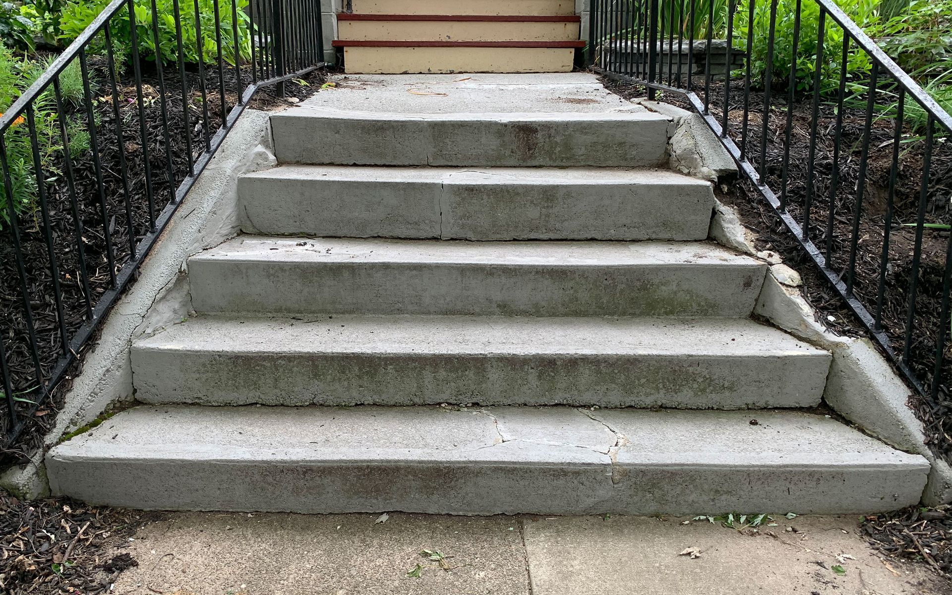 A set of concrete stairs with a metal railing leading up to a house.