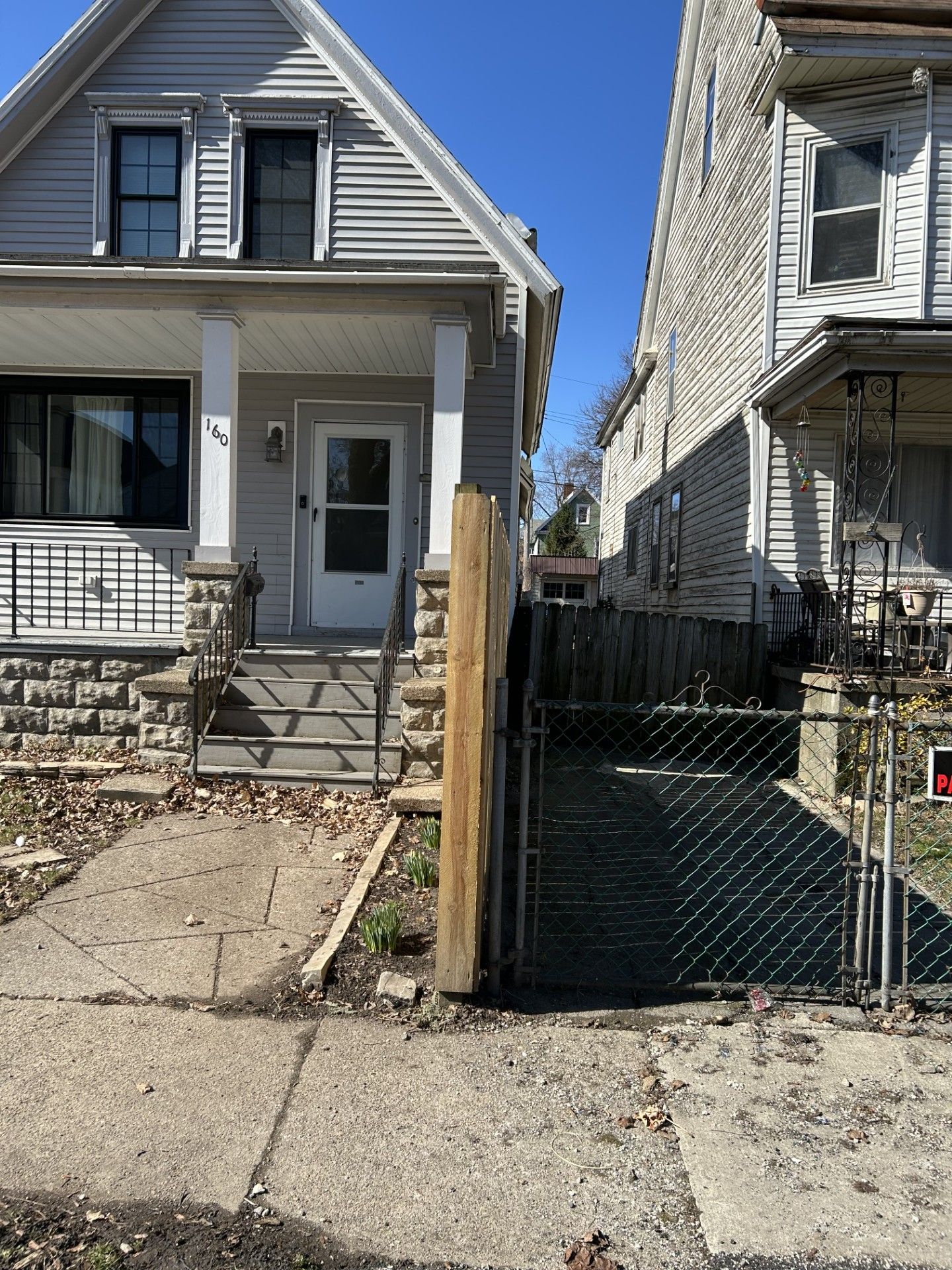 A brick house with a rocking chair in front of it and a concrete walkway leading to the front door.