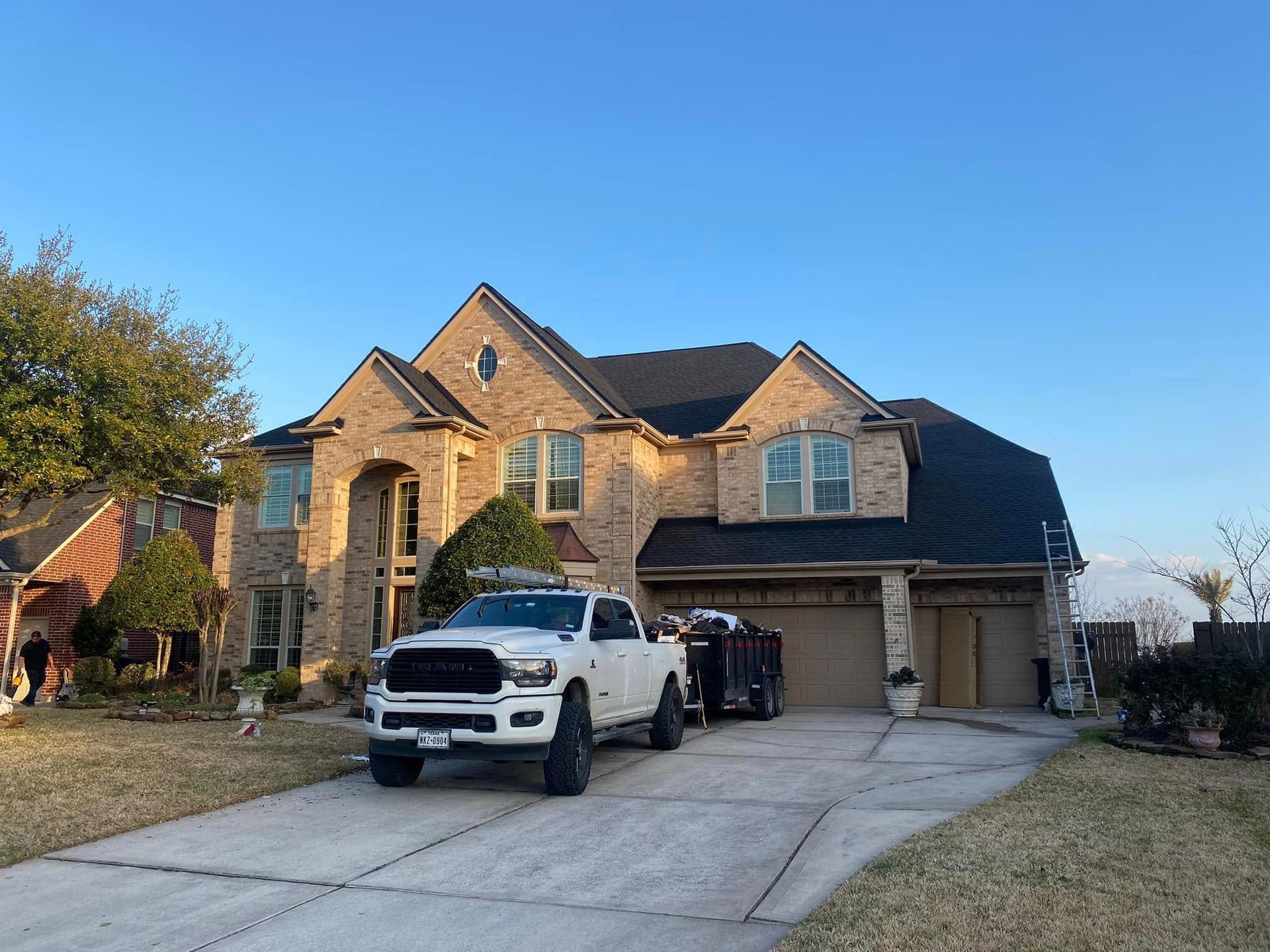 White pickup truck with a trailer parked in front of a brick house. Sunny day, clear sky.