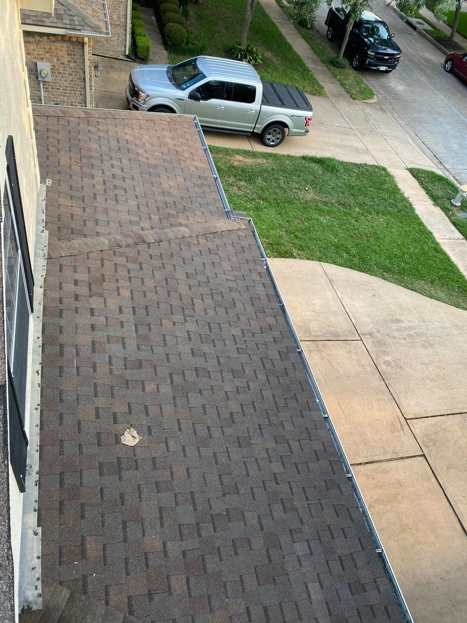 Brown shingled roof with a silver truck parked in a driveway next to a grass area and a street.