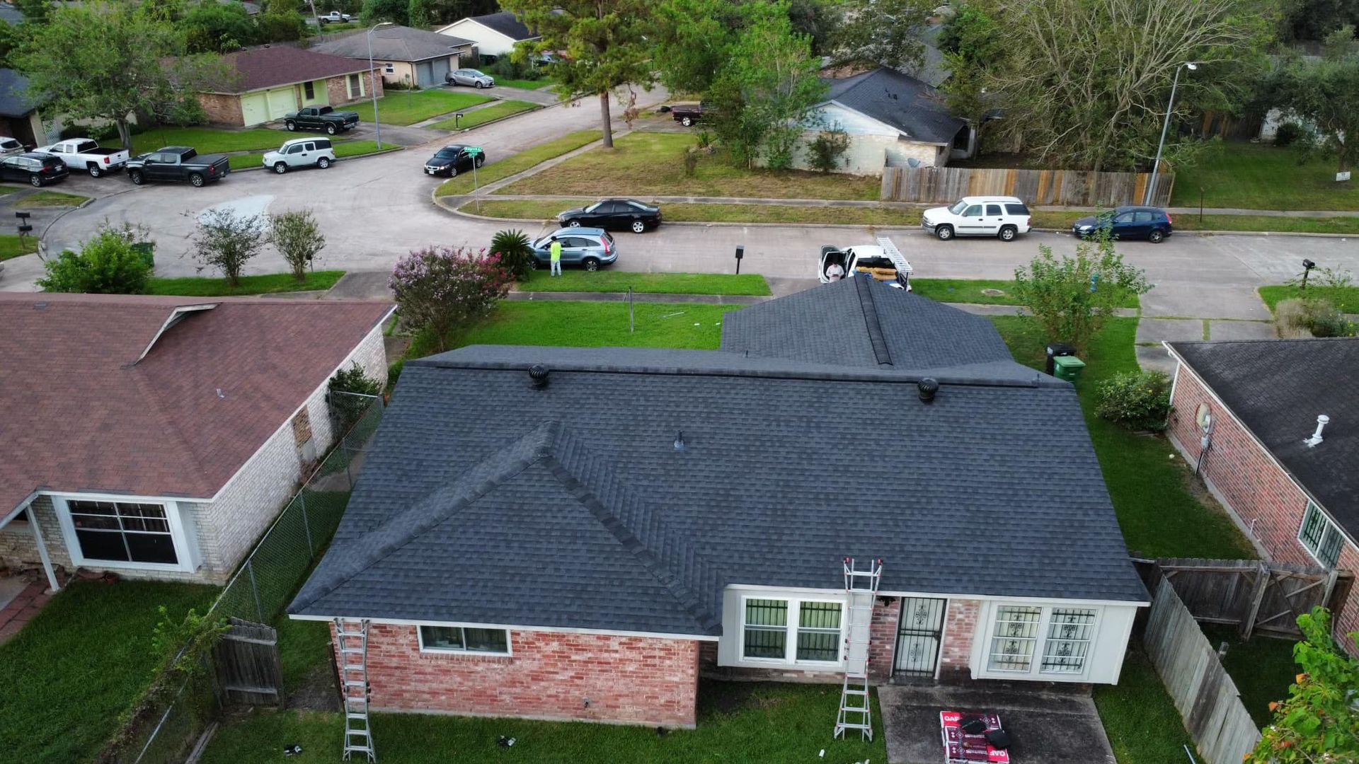 Aerial view of a house with a newly shingled roof, surrounded by other houses and a street.