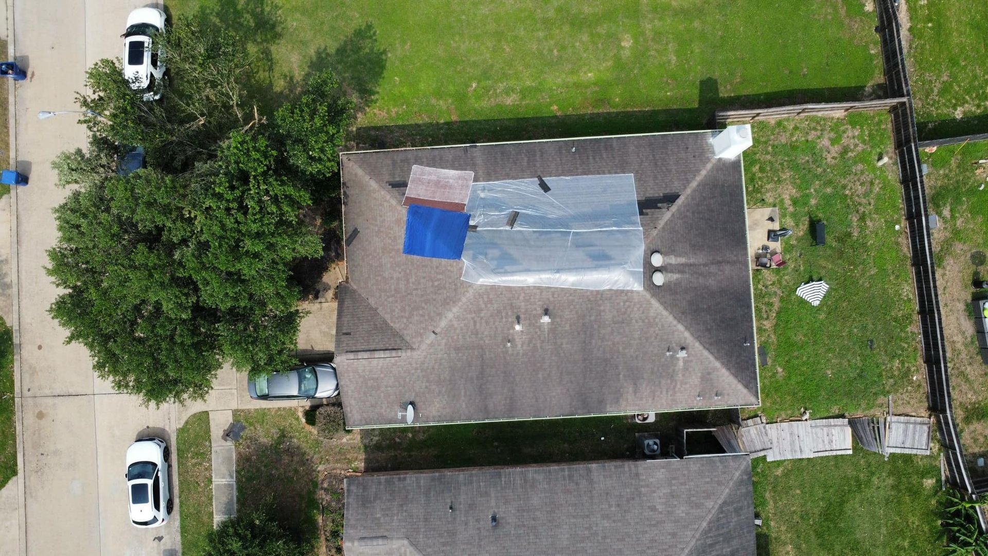 Overhead view of a house roof partially covered with blue and gray tarps, likely for repairs.