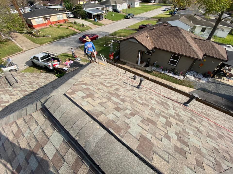 Roofer on a residential roof working with a truck and supplies nearby in a sunny neighborhood.