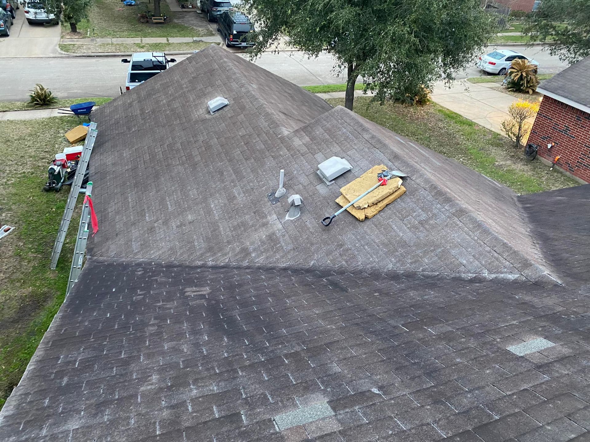 Dark, weathered rooftop with equipment, ladder, and trees; residential neighborhood.