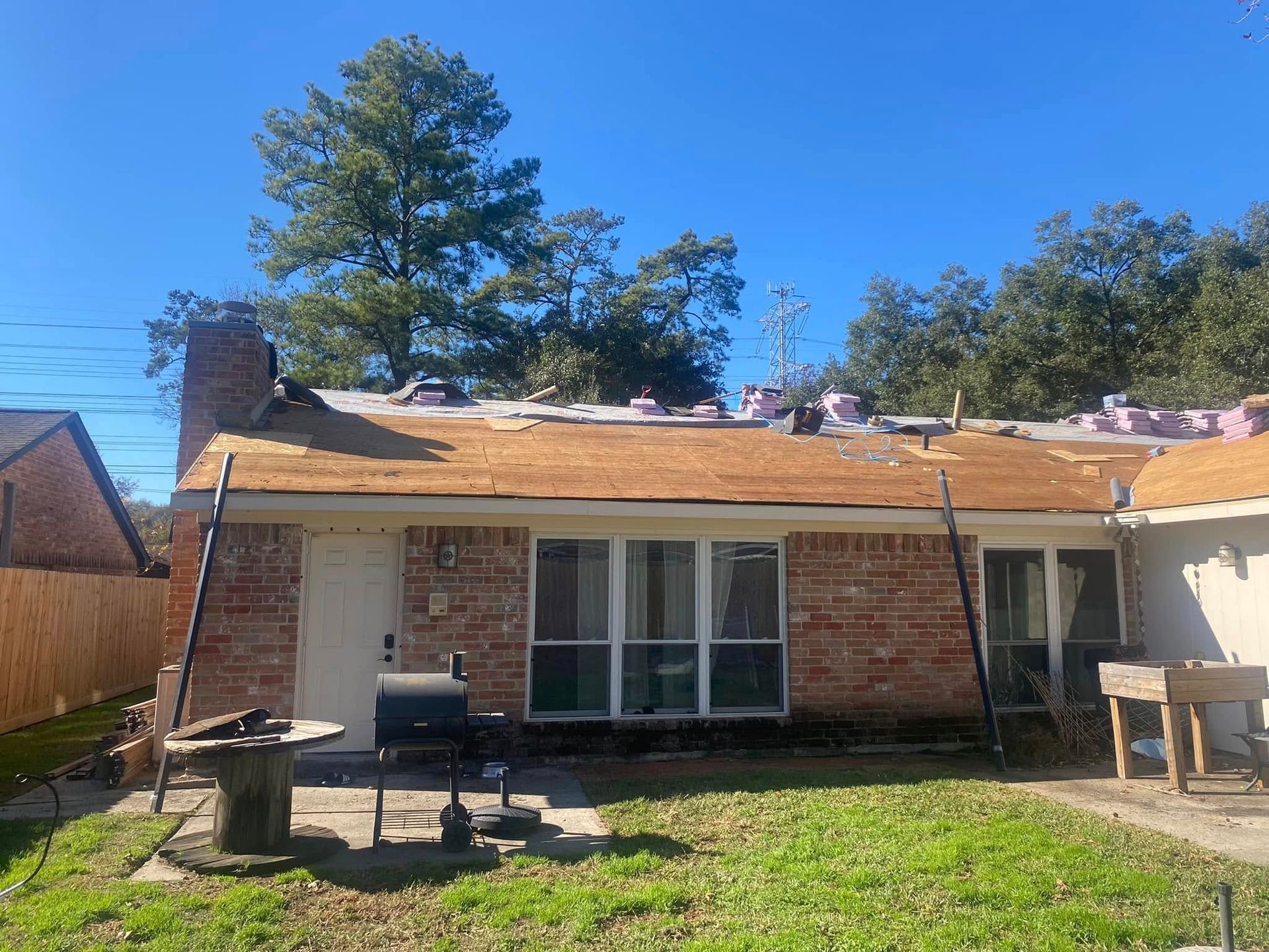 House with roof under construction, visible wood underlayment and chimney. Sunny day.
