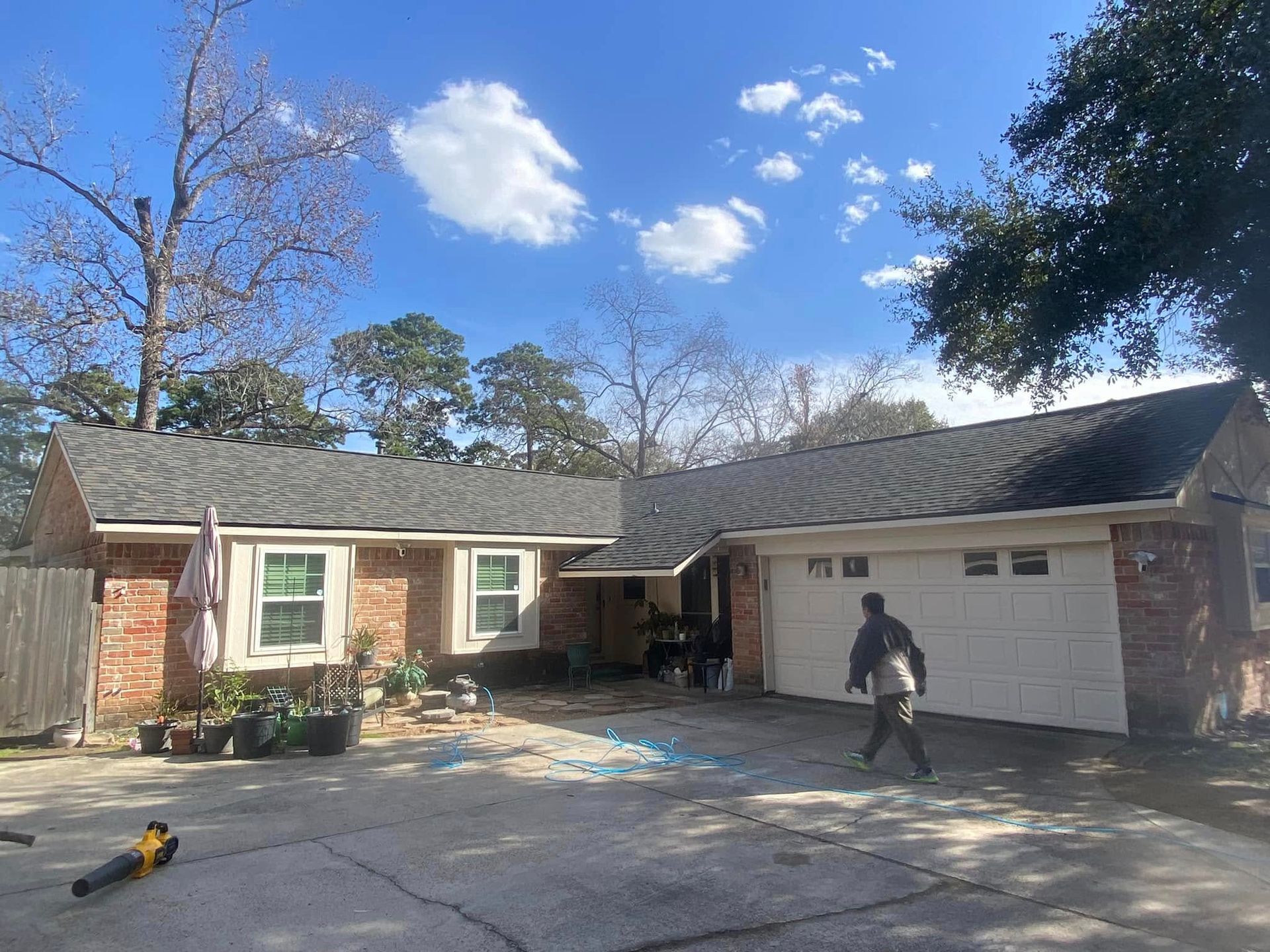 Brick house with a newly shingled roof, person walking on driveway.