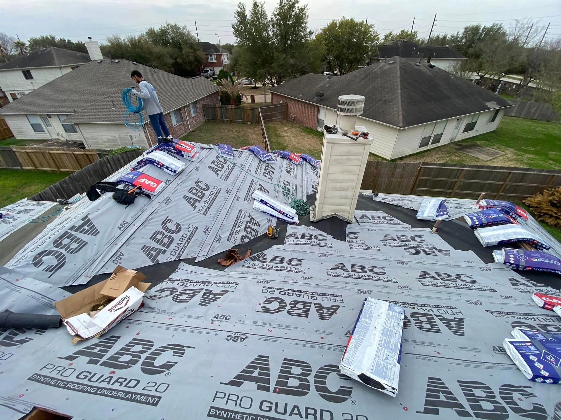 Roofing work in progress; person on ladder, roof covered in underlayment with building materials.
