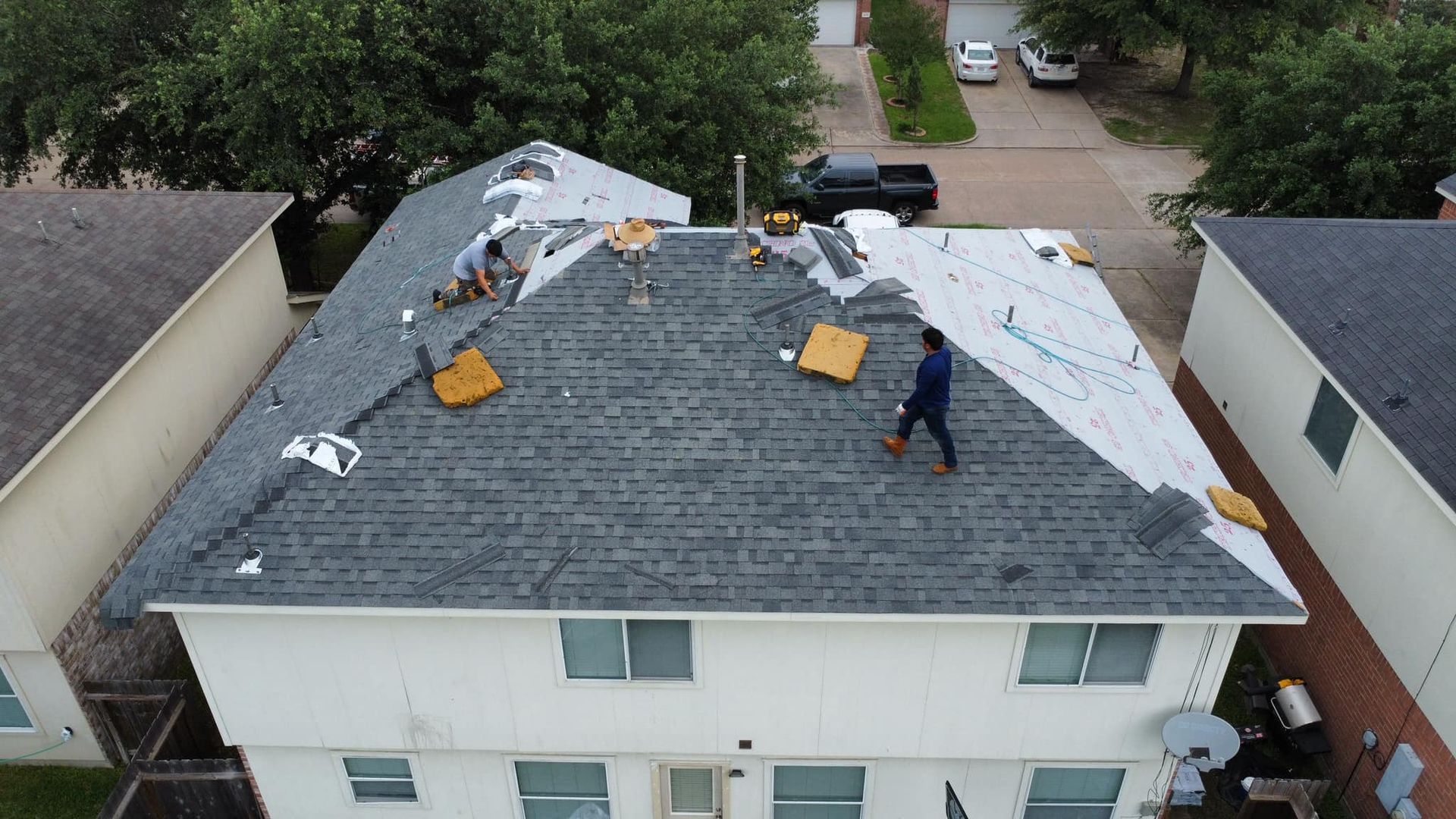 Roofers working on a residential house roof, partially stripped and covered with tarps.