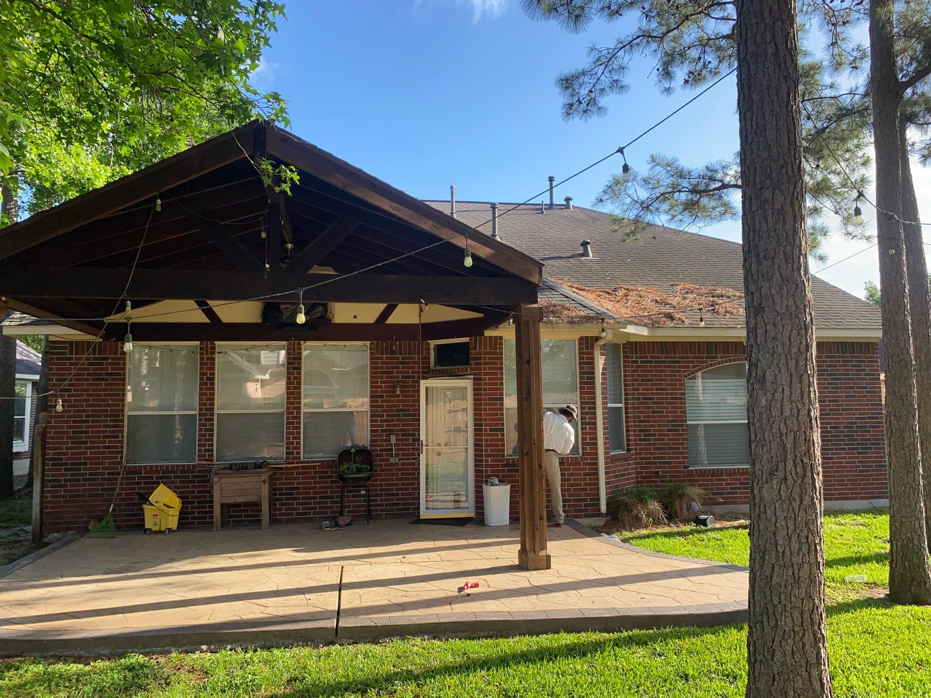 Brick house with patio and covered area, string lights, trees, and sunny sky.
