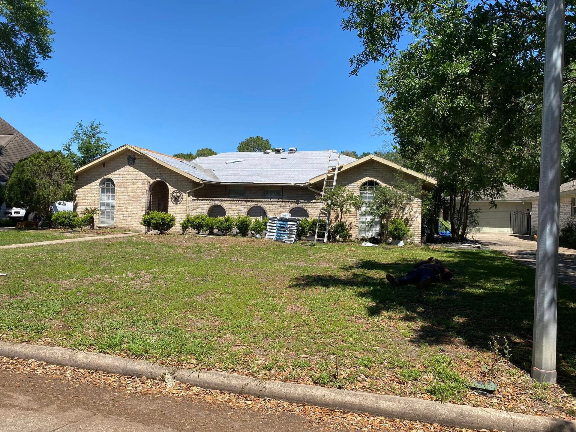 Single-story brick house with damaged roof and debris on the lawn on a sunny day.