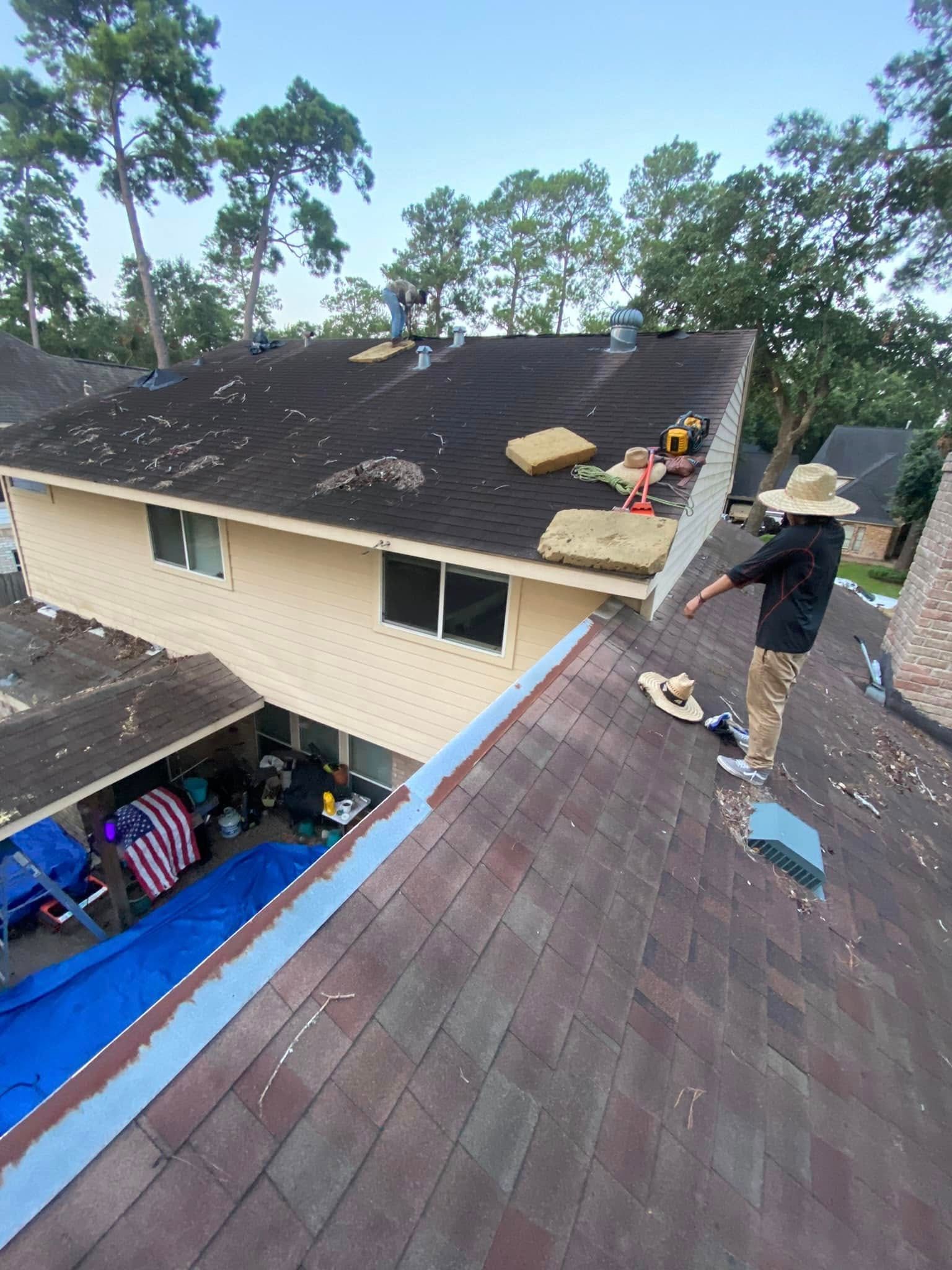 A person on a roof points towards roofers working. House with pool, blue tarp, and trees in the background.