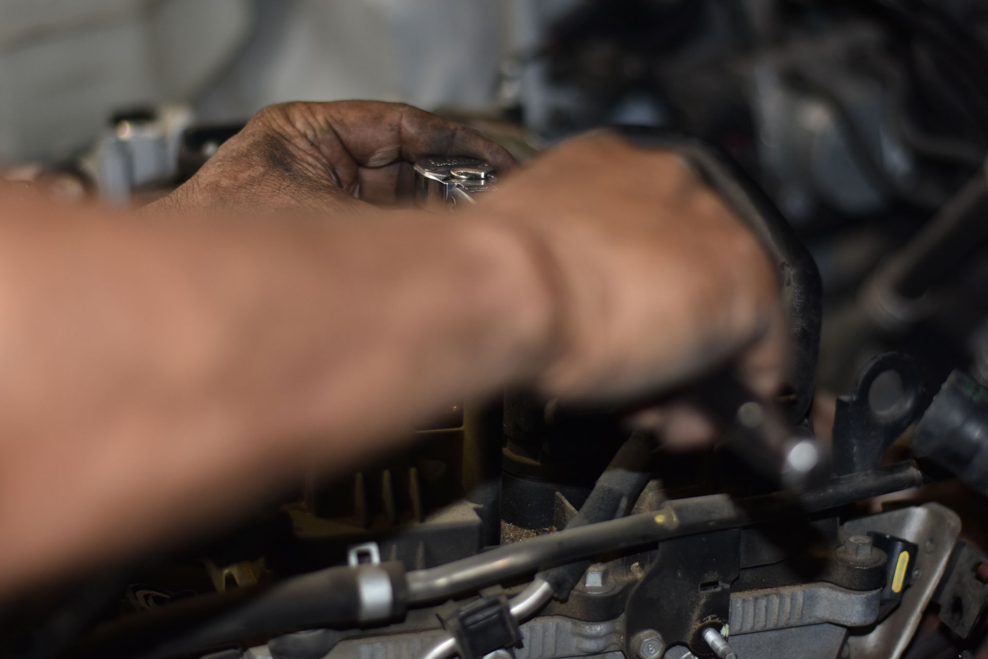 Mechanic's hands working on a car engine, using tools in a garage.