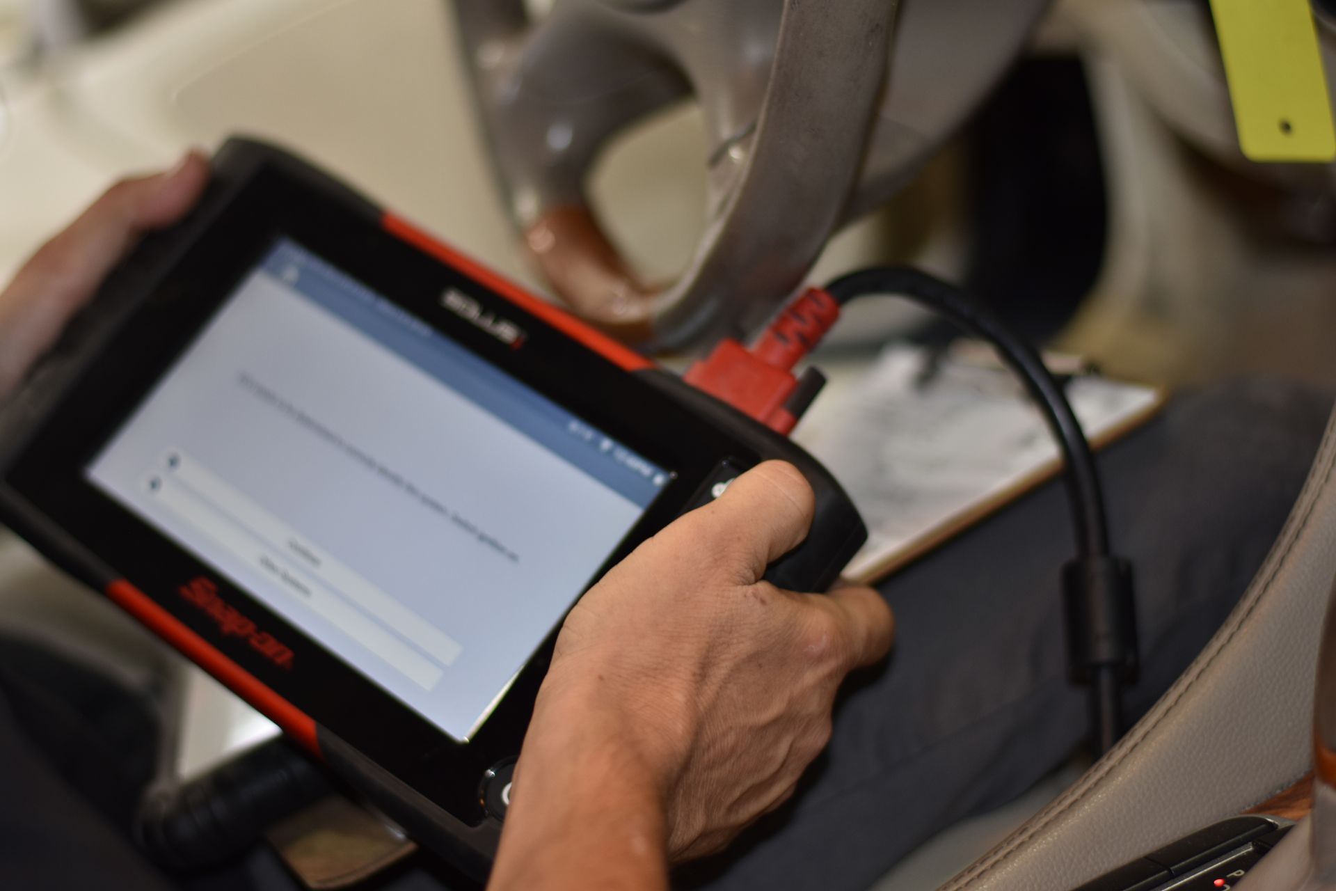 Person using a Snap-on diagnostic tool, connected to a vehicle, likely troubleshooting in a garage setting.