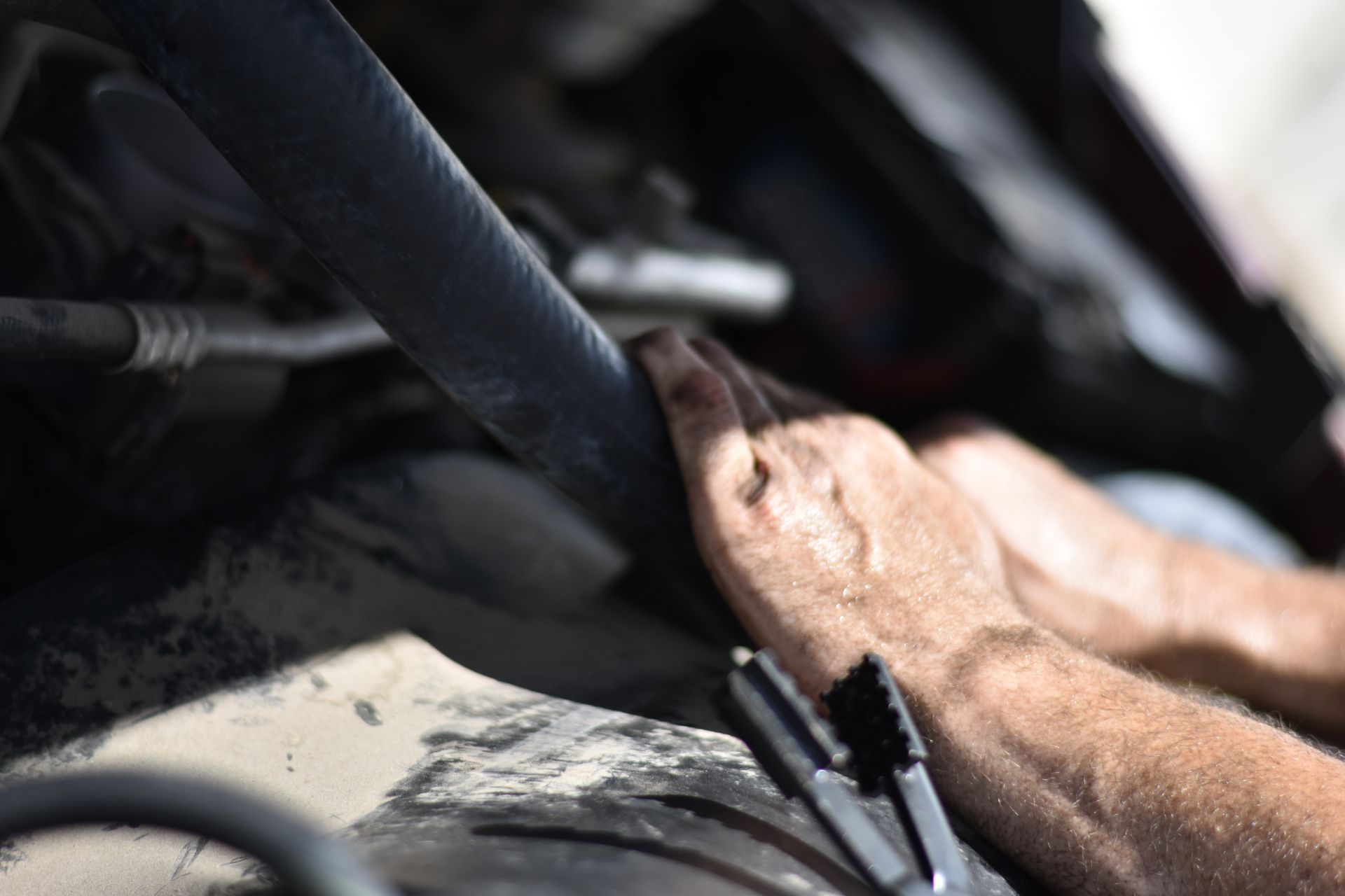 Hands working on a car engine, holding a hose with pliers in the foreground.