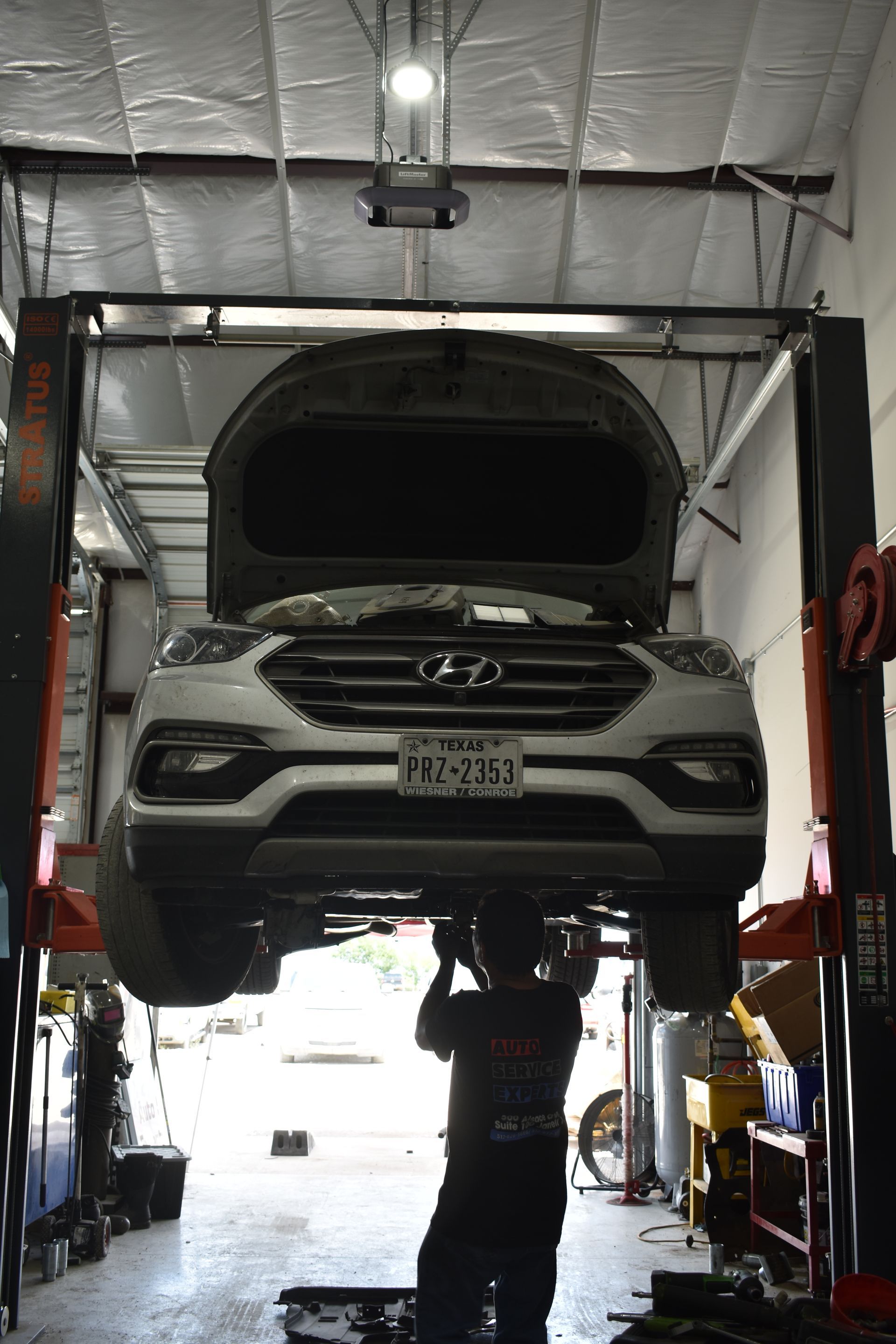 A car on a lift in a garage, a mechanic is working underneath.