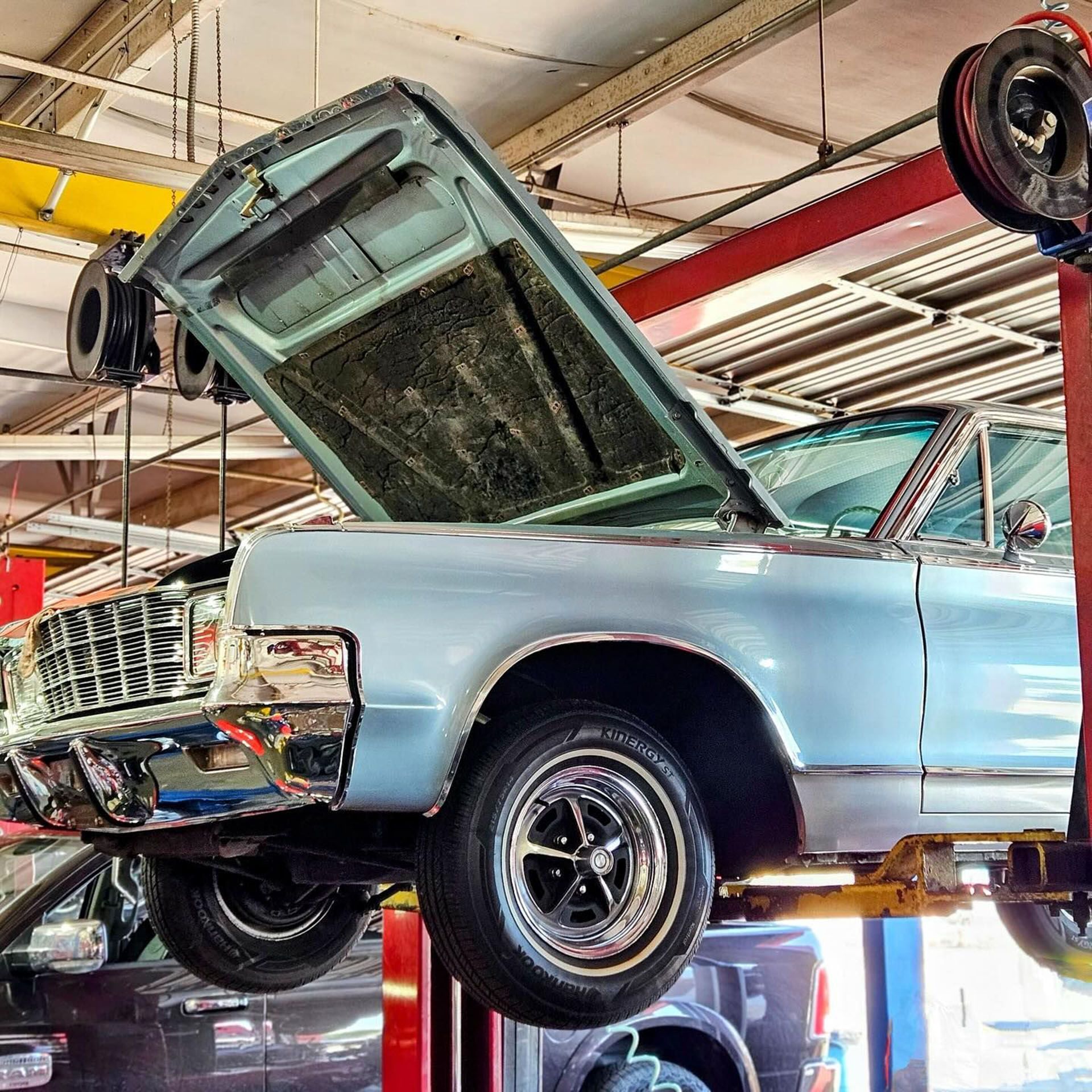 A car with the hood open is on a lift in a garage.
