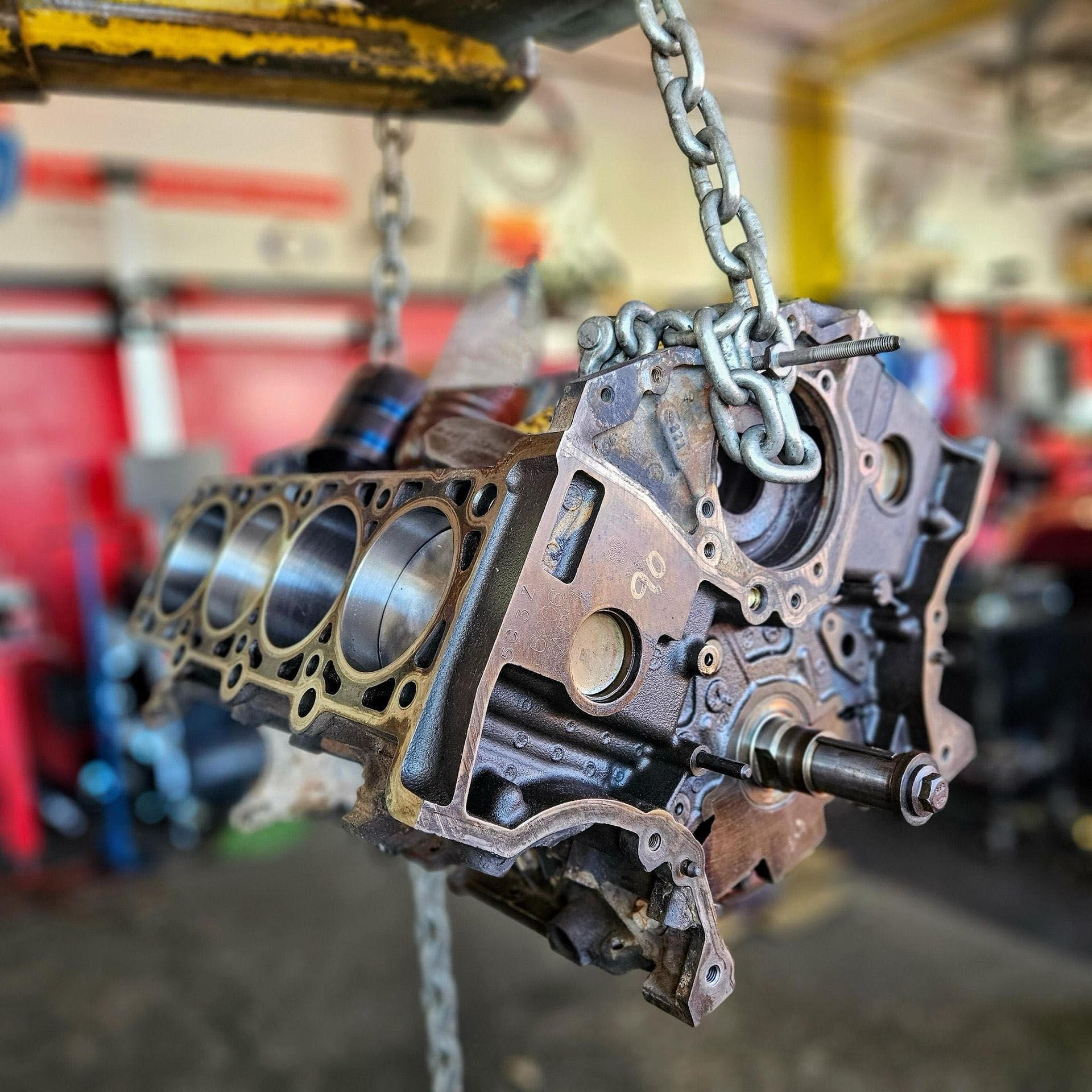 A close up of a engine block hanging from chains in a garage.