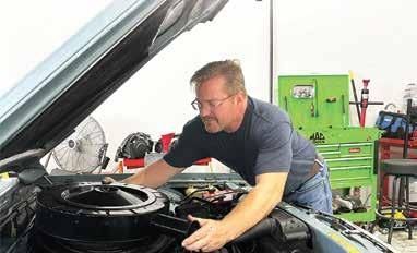 Man in a workshop leaning over an open car engine, inspecting parts under the hood