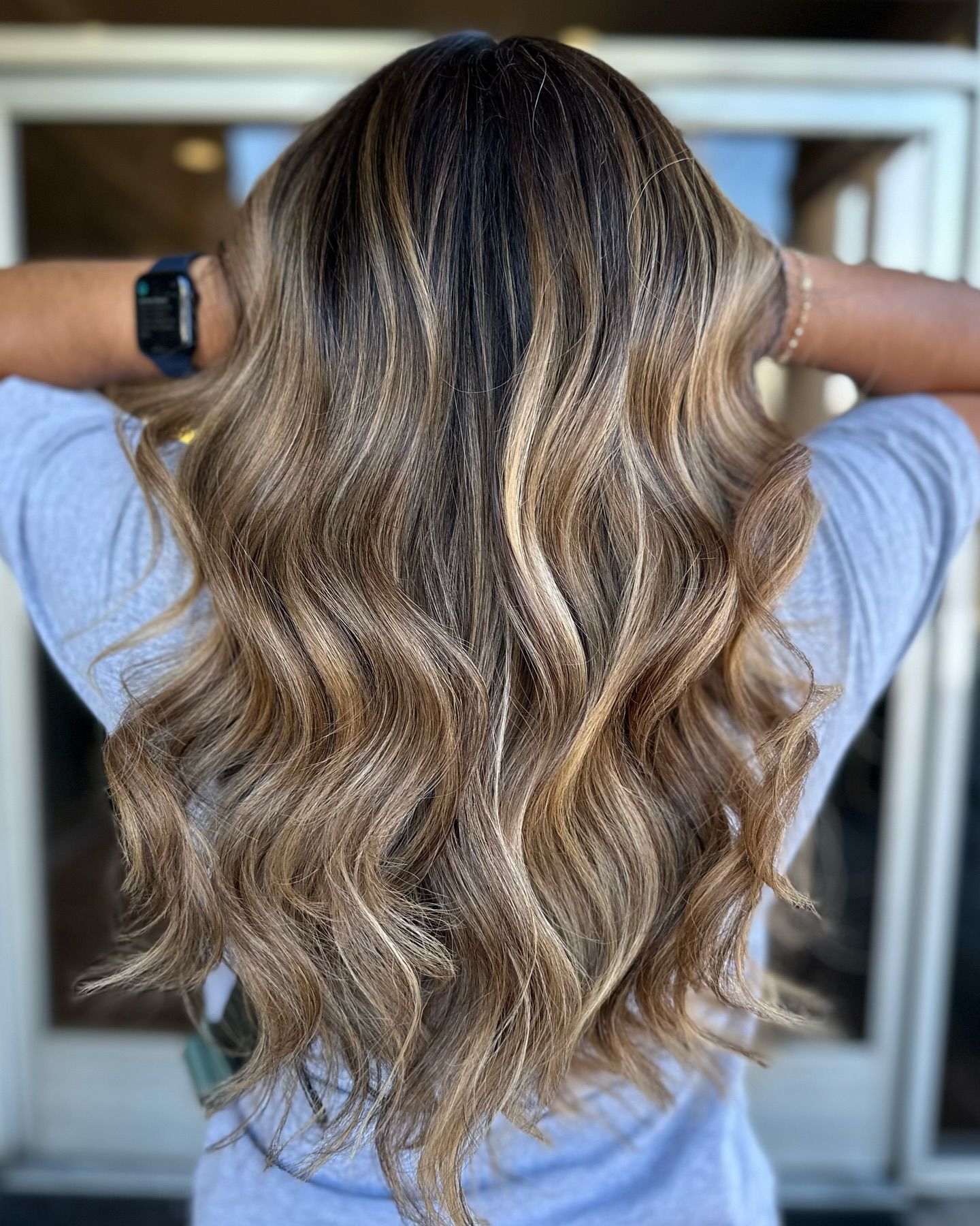 A woman with long wavy hair is wearing a watch and a gray shirt.
