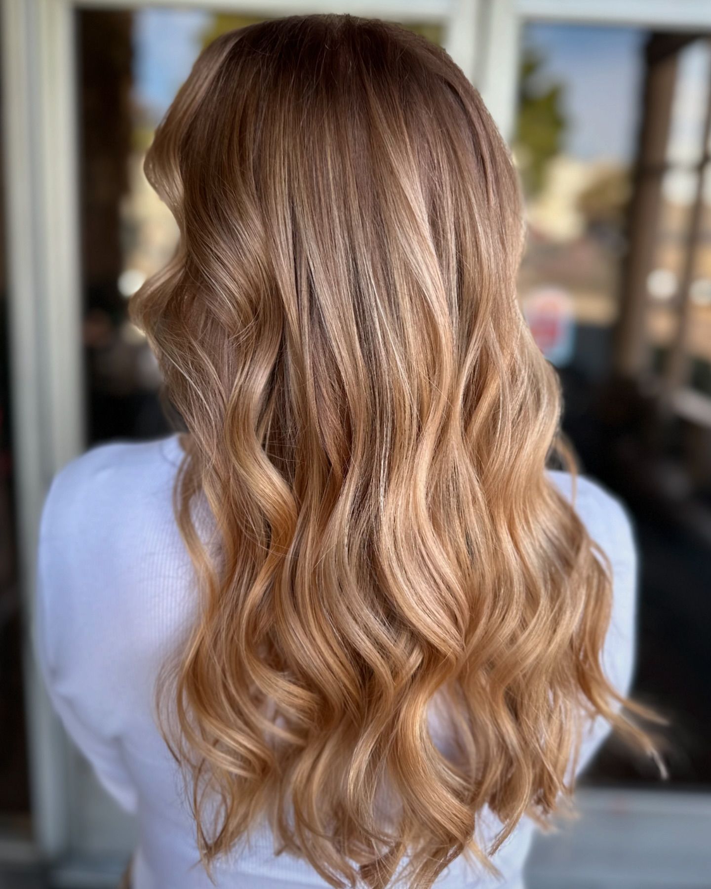 A woman with long blonde hair is wearing a white shirt and standing in front of a window.