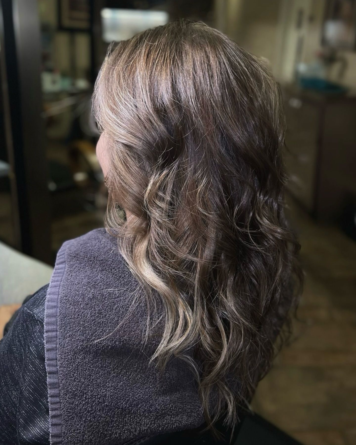 A woman with long brown hair is sitting in a chair with a towel around her neck.