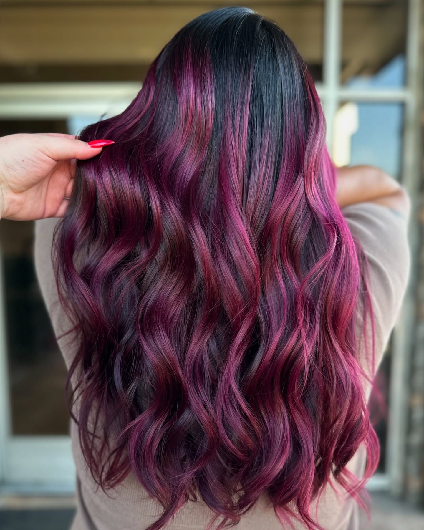A woman with long purple hair is standing in front of a building.