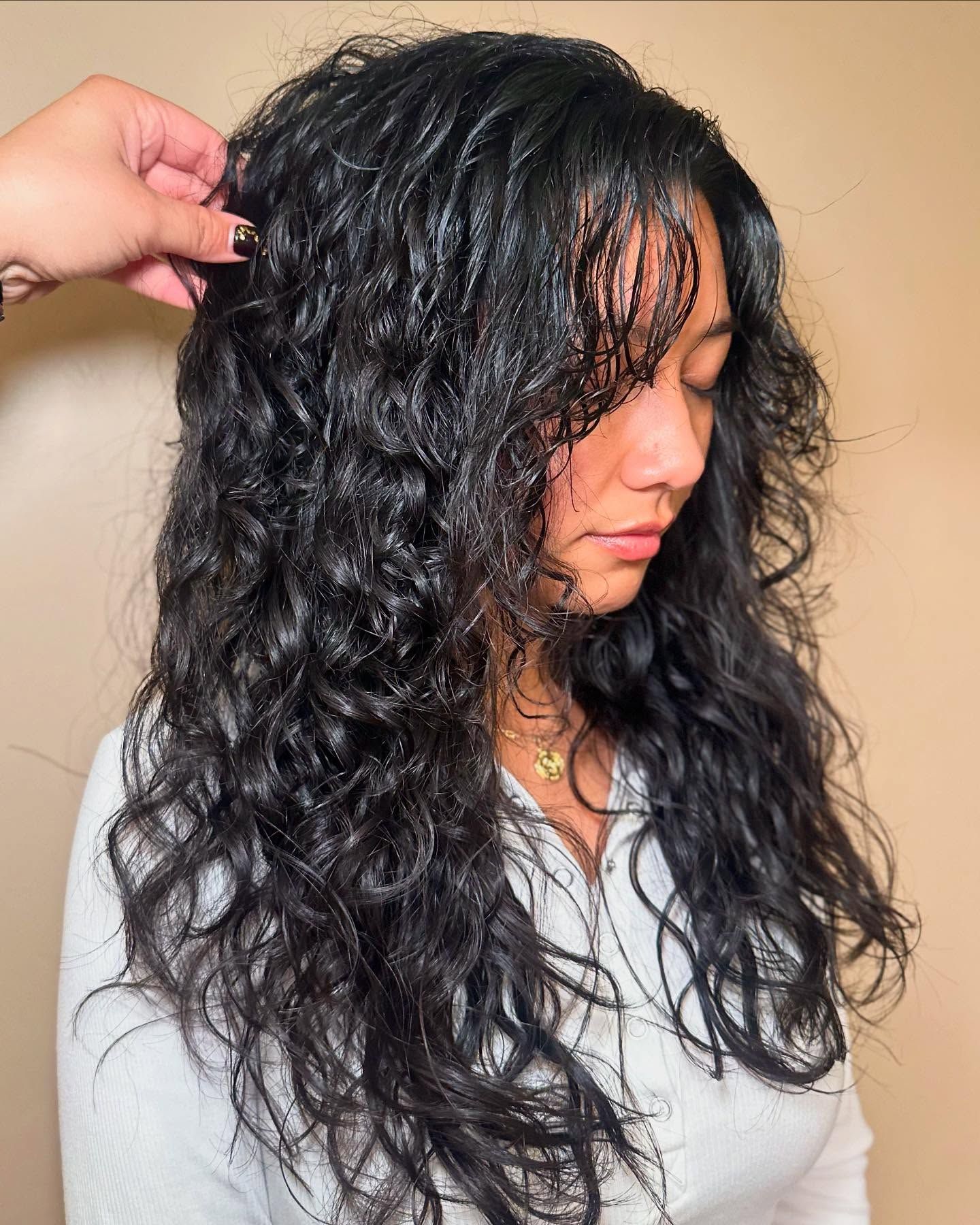 A woman with long curly hair is getting her hair done by a hairdresser.