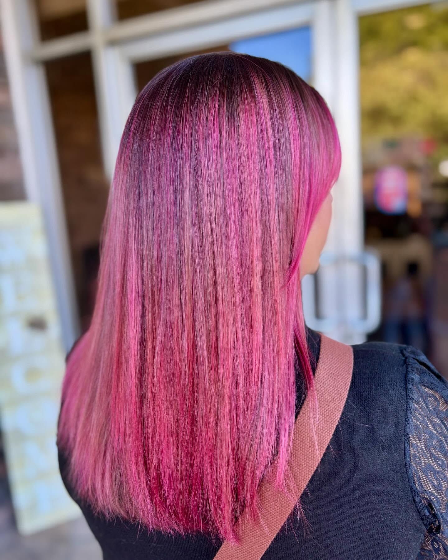 A woman with long pink hair is standing in front of a building.
