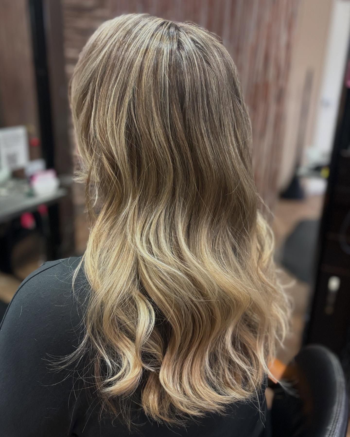A woman with long blonde hair is sitting in a chair in a salon.