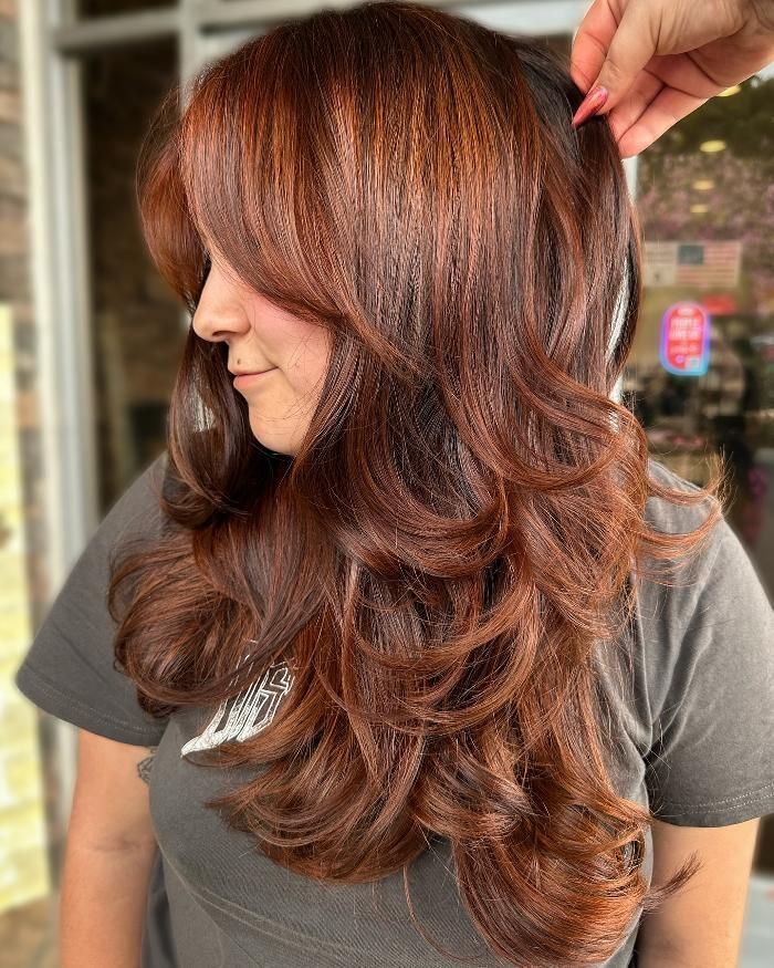 A woman with long brown hair is getting her hair cut.