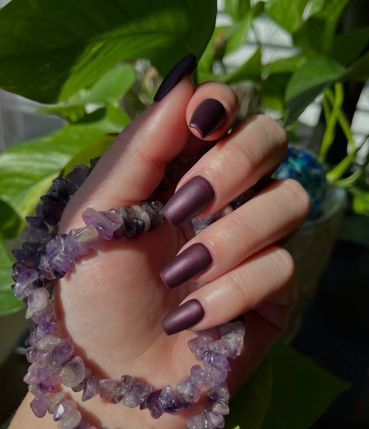 A woman 's hand with purple nails is holding a purple bracelet.