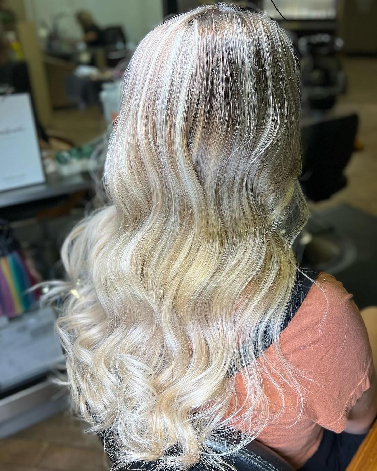 A woman with long blonde hair is sitting in a chair in a salon.