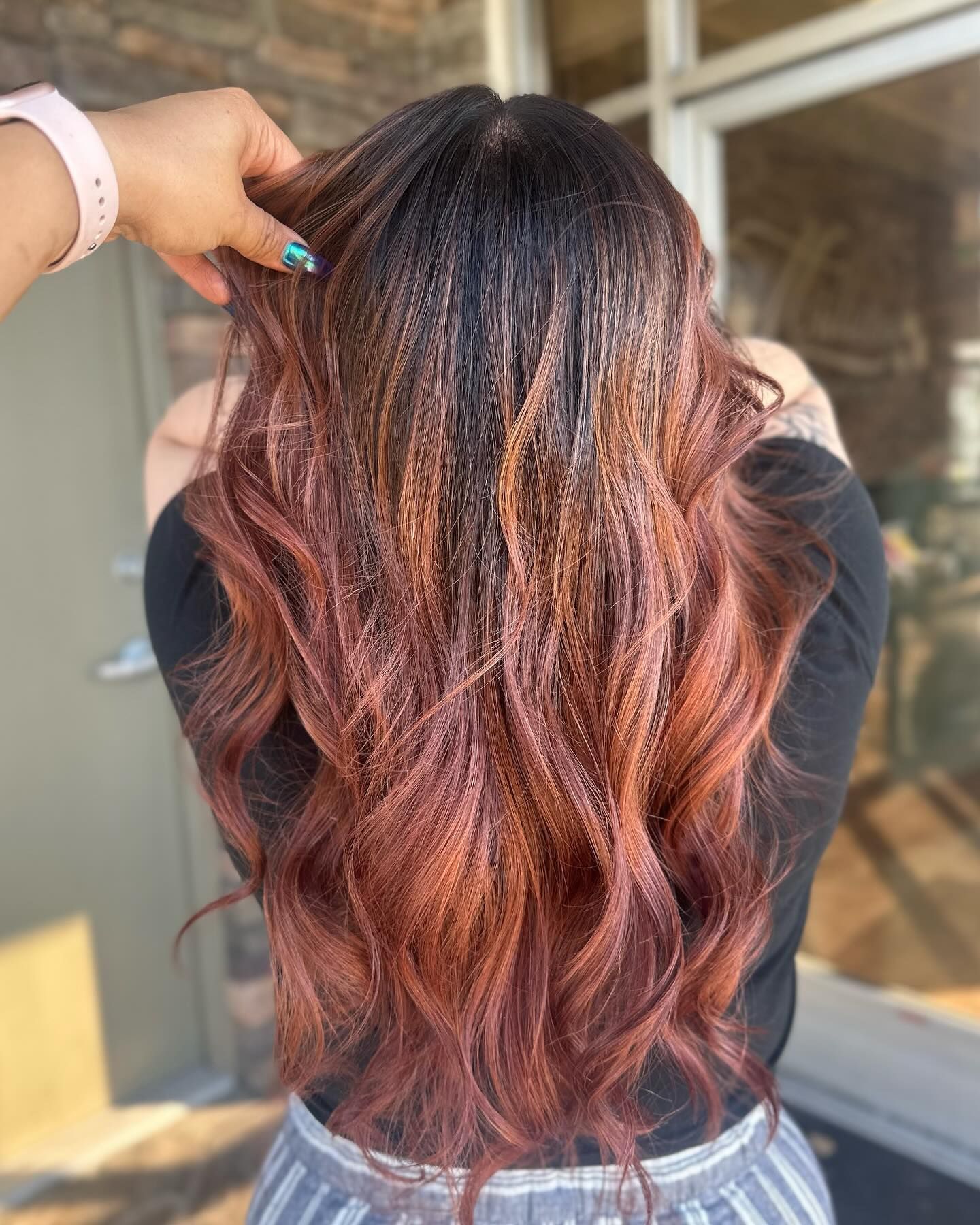 A woman with long red hair is standing in front of a window.